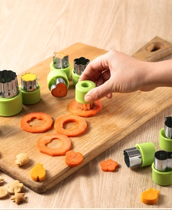 Hand using a stainless steel cookie cutter set to slice carrots on a wooden board