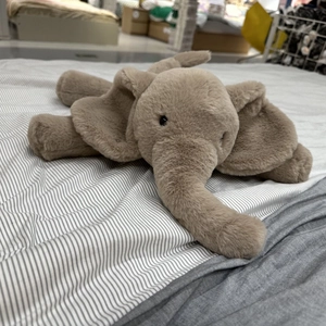 Soft plush elephant stuffed animal toy in light brown lying down on a cozy bed