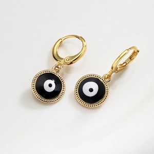 Golden hoop earrings with black and white evil eye pendants on a reflective surface