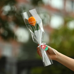 Macro shot of a handmade orange knitted tulip wrapped in plastic with a gift tag