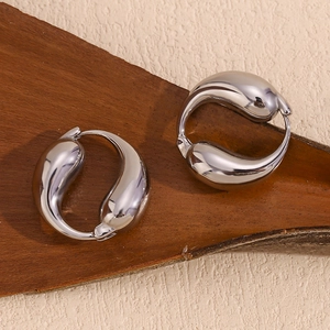 Close-up of silver-tone teardrop earrings on bark, showing smooth polished metal surface