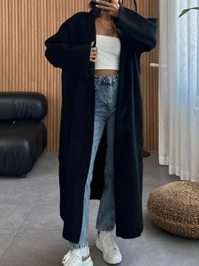 Gros plan sur un manteau long noir en maille avec crop top blanc et jean en denim bleu
