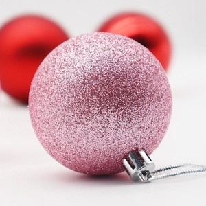 Pink glitter Christmas ball ornament with silver cap and string on festive background