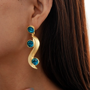 Close-up of elegant gold S-shaped wave earrings featuring three round blue crystals