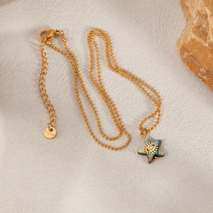 Gold stainless steel star necklace with abalone evil eye pendant on a grey surface