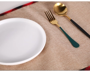 Close-up of golden stainless steel cutlery with green and black handles on linen mat