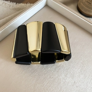 Detail of wide geometric acrylic bracelet with matte black and mirror gold panels