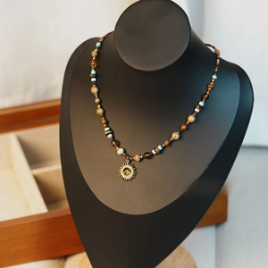 Détail du collier perlé avec pendentif soleil doré sur support de bijoux noir