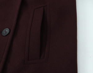 Detail of dark wine red wool coat featuring a vertical pocket and black matte button