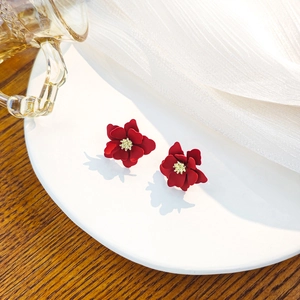 Elegant deep red floral stud earrings with gold center on a white ceramic plate