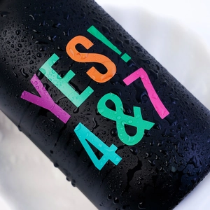 Macro detail of black matte sports bottle with colorful Yes 4&7 text and water droplets
