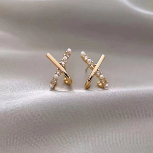 Macro shot of gold crisscross X earrings featuring white pearls and zircon on silk background
