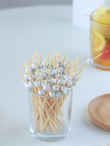 Close-up of bamboo cocktail picks with white soccer ball beads in a glass