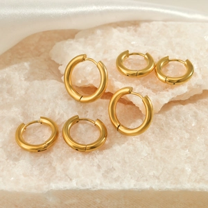 Three pairs of thick minimalist gold hoop earrings set on white crystal and silk fabric