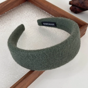 Close-up of green wool texture headband with a white handmade label on a wooden tray