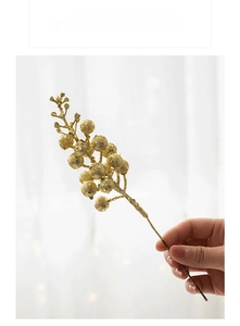 Detail einer Hand, die einen goldenen Glitzer-Beerenstiel für die Weihnachtsdeko hält