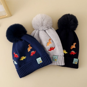 Détail de bonnets tricotés pour garçons avec broderie dinosaure et pompons en fausse fourrure