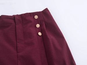 Detail view of burgundy trousers featuring elegant waist pleats and three gold side buttons