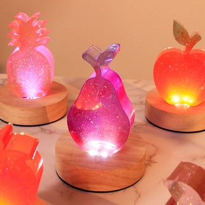 Luminous fruit-shaped resin molds set with pineapple, pear, and apple on wooden base
