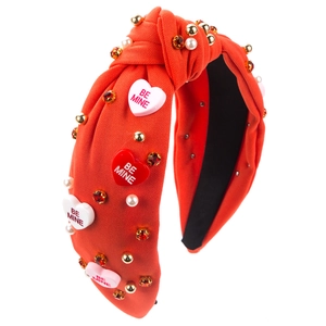 Détail d'un serre-tête noué rouge avec perles, strass et breloques en forme de cœur