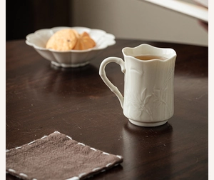 Detail of white ceramic coffee mug with floral embossed texture on dark wood table