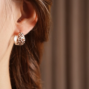 Close-up of silver hollow patterned hoop earring worn by a model in a side view