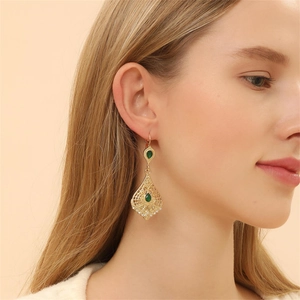 Close-up of vintage gold teardrop earrings with green stones worn by a model