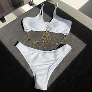 Close-up of white bikini with wavy texture and decorative gold chain tassel accents