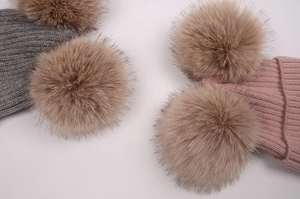 Détail de bonnets en tricot gris et rose avec deux grands pompons en fausse fourrure