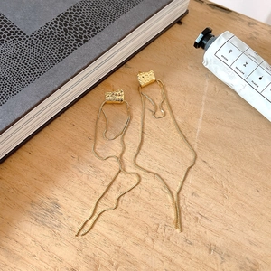 Detail of gold fringe earrings with irregular hammered texture on a wooden surface