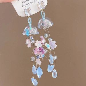 Detail of floral resin earrings with long tassels and blue crystals on a card