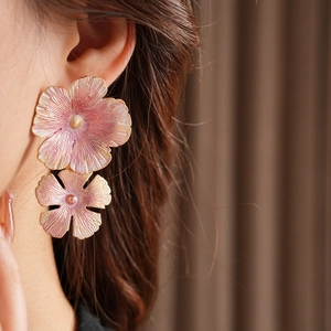 Close-up of pink and gold floral enamel earrings featuring double-layered petal texture