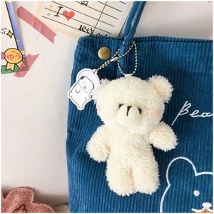 Close-up of cute white plush bear charm with acrylic astronaut tag on corduroy tote bag