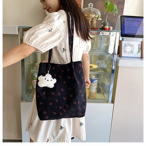 Detail of black corduroy tote bag with strawberry embroidery and plush keychain on model