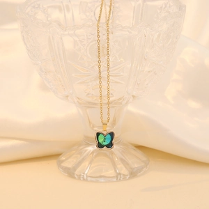 Golden chain necklace with a green crystal butterfly pendant on soft white silk background