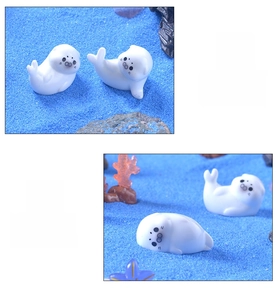 Macro detail of miniature white seal figurines on blue sand with coral decorations