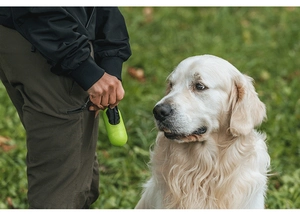 Handheld green capsule pet waste bag dispenser with LED light on a natural lawn background