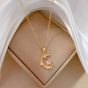 Close-up of gold moon necklace with pink heart and clear stones on beige display pad