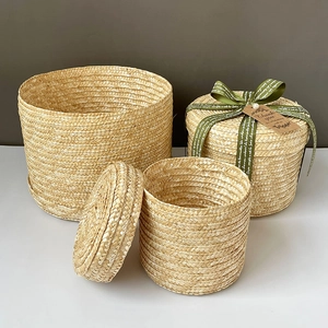 Set of three round woven straw gift boxes with lids and green ribbons in natural finish