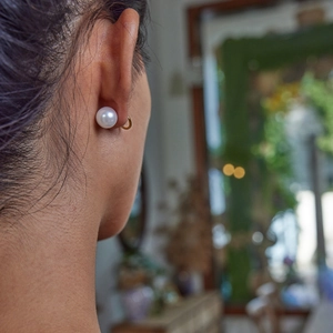 Close-up of white round pearl earrings on model with elegant gold stud settings