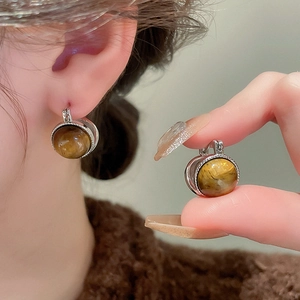 Detail of silver tiger eye earrings with brown gemstone on model and held in hand