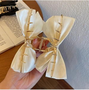 Detail of a large cream satin bow hair claw clip with golden metal grip shown in hand
