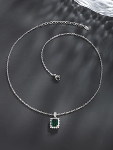 Macro detail of silver necklace with square green gemstone surrounded by white zircons