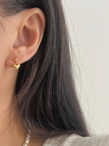 Close-up of heart-shaped gold stud earring with a sparkling zircon on model's ear