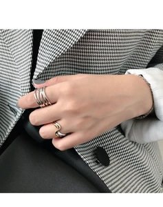 Detail showing layered silver and two-tone wavy rings on a hand in houndstooth jacket