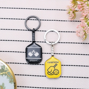 Black and yellow pickleball racket metal keychains set on a grid pattern background