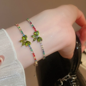 Close-up of stacked silver bracelets with green zircon butterfly charms on a wrist