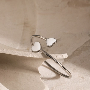 Detail of silver stainless steel open bangle with two white enamel heart-shaped ends