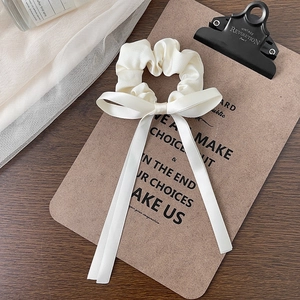 Detailed macro view of a cream-colored satin bow scrunchie on a vintage clipboard