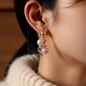 Close-up of elegant gold earrings with white and pink pearls on a model's ear
